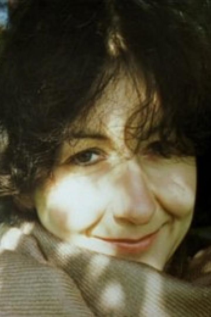 Eine lächelnde Frau mit dunklen Haaren und einem Schal im Freien.