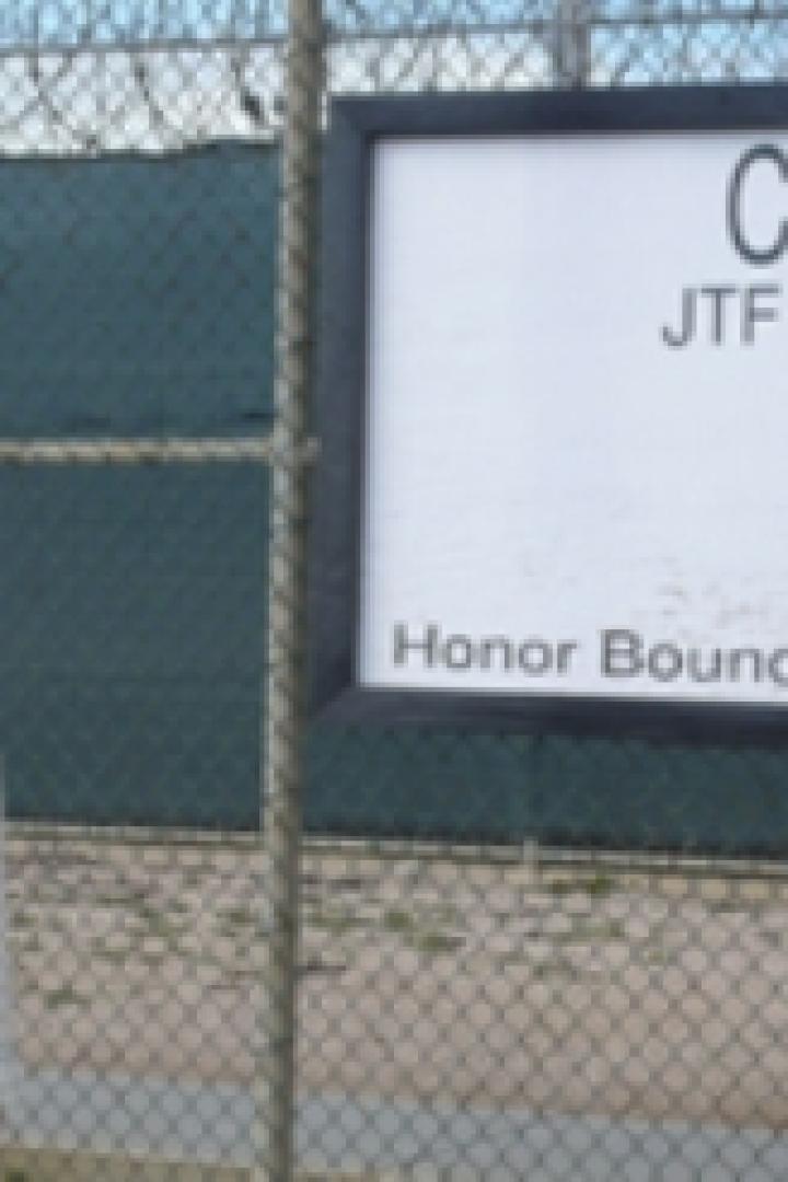 Ein Mann steht vor einem Schild mit der Aufschrift „Camp VI JTF Guantanamo“.