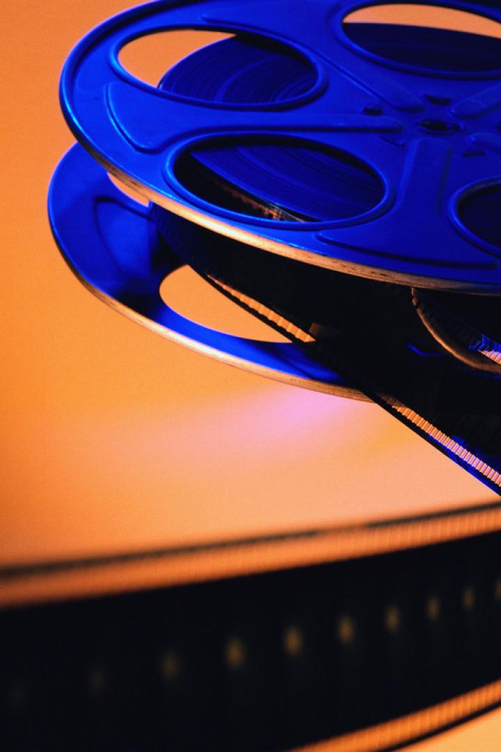 Eine blaue Filmrolle mit einem aufgewickelten Filmband vor einem orangefarbenen Hintergrund.