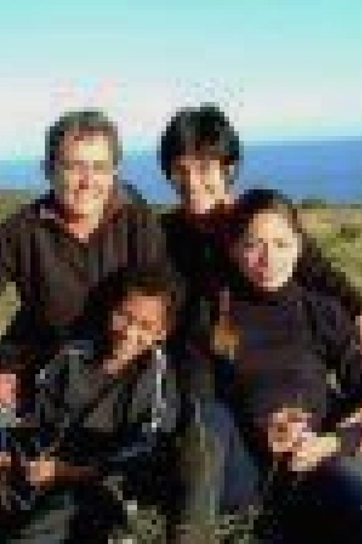 Eine Gruppe von vier Personen sitzt auf einer Wiese mit Blick auf das Meer.