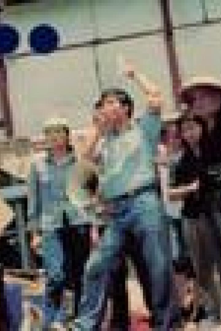 Eine Menschenmenge steht im Freien, einige gestikulieren und halten Schilder hoch.