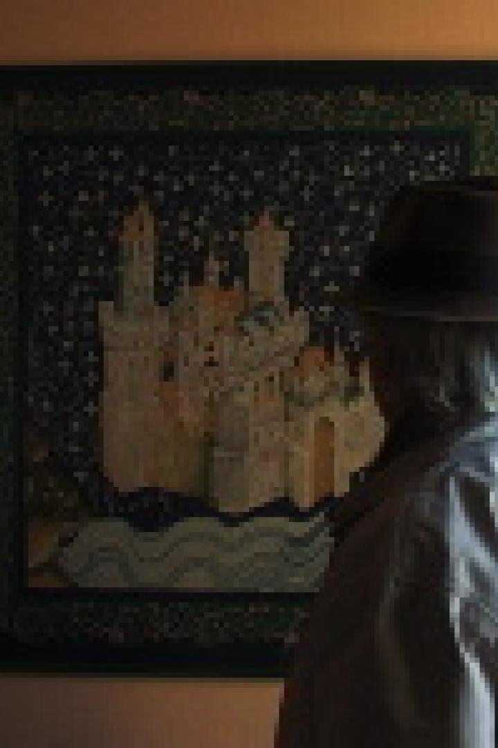 Eine Person mit Hut betrachtet ein gerahmtes Bild eines Schlosses.