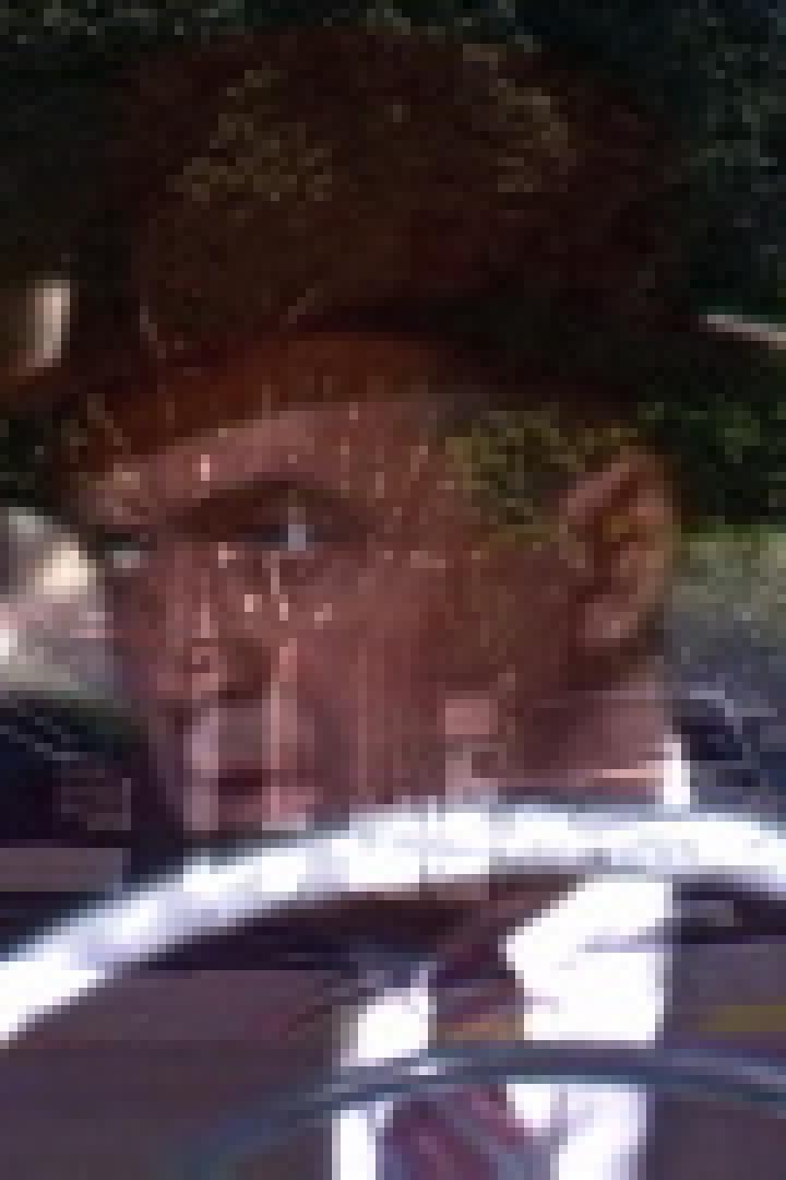 Ein Mann mit Hut fährt ein Auto auf einer sonnigen Straße.