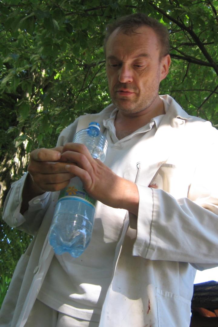 Ein Mann im weißen Kittel betrachtet eine Plastikwasserflasche unter einem Baum.