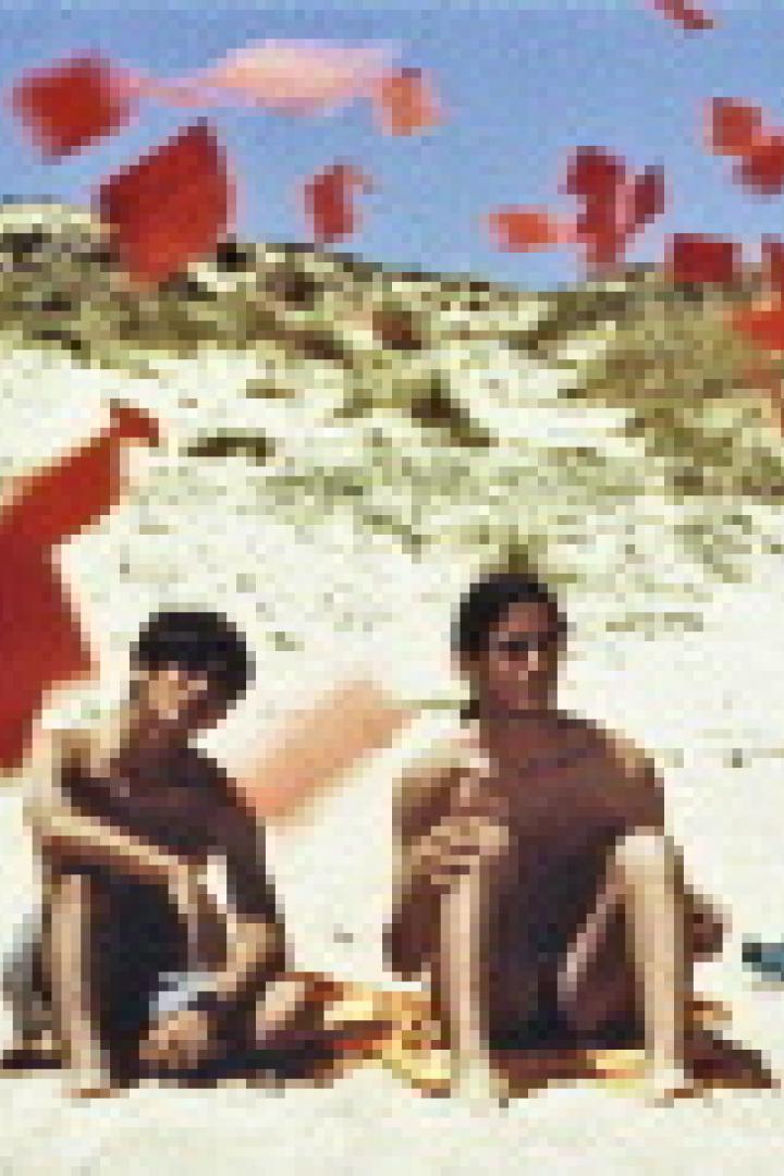 Drei Personen sitzen und stehen an einem Strand, während rote Papierstücke in der Luft schweben.