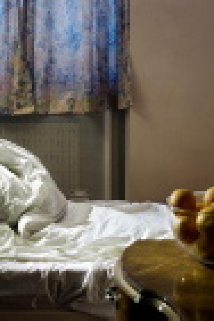 Ein ungemachtes Bett steht in einem Zimmer, auf einem Tisch daneben steht eine Schale mit Orangen.