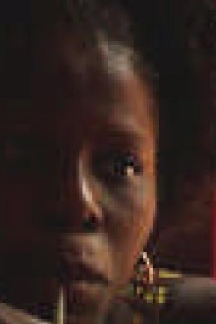 Eine Frau mit dunkler Haut und lockigem Haar vor einem roten Hintergrund.