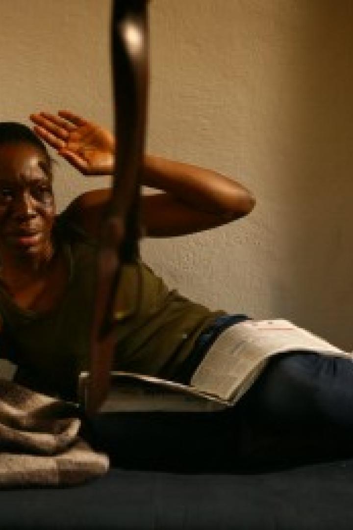 Eine verängstigte Frau liegt mit einem Buch auf einem Bett und hält die Hände schützend vor das Gesicht.