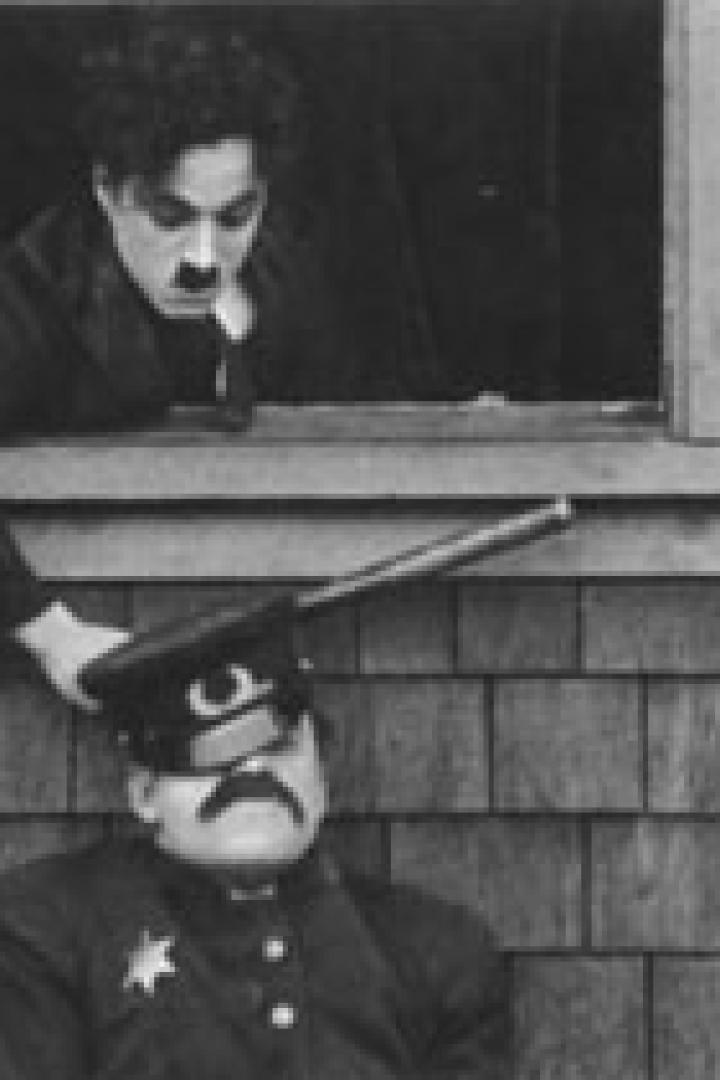 Charlie Chaplin zielt mit einem Gewehr auf einen schlafenden Polizisten.