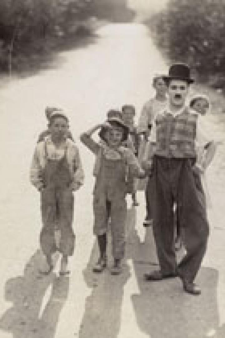 Charlie Chaplin geht mit einer Gruppe von Kindern auf einer Landstraße.