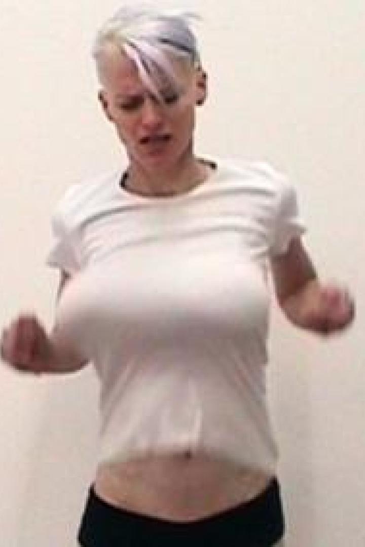 Eine Frau mit kurzen, blonden Haaren und einem weißen T-Shirt tanzt vor einer weißen Wand.