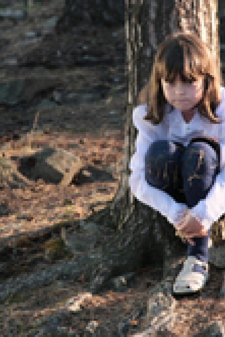 Ein trauriges Mädchen sitzt an einem Baum im Wald.