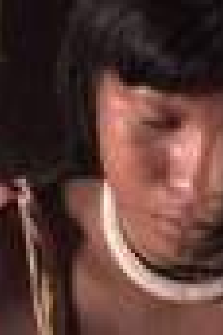 Eine indigene Frau mit dunklen Haaren und einem weißen Halsband blickt nach unten.