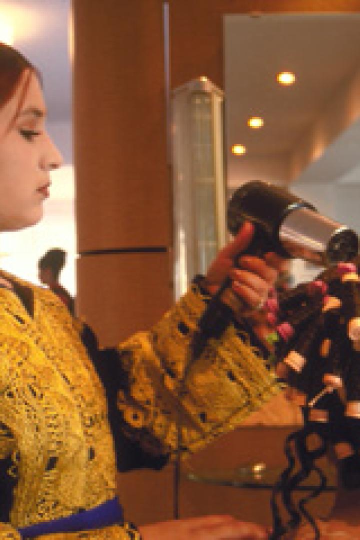 Eine Frau mit traditioneller Kleidung föhnt die Haare einer anderen Frau mit Lockenwicklern.