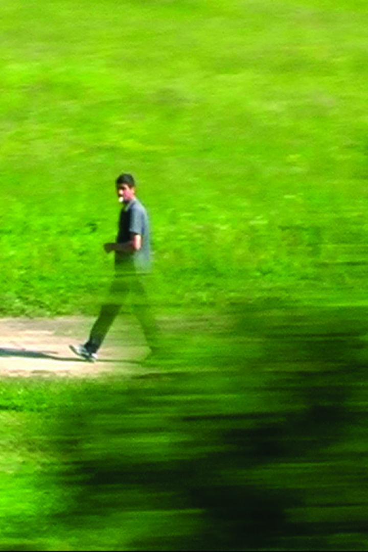 Ein Mann geht auf einem Feldweg durch eine grüne Landschaft.