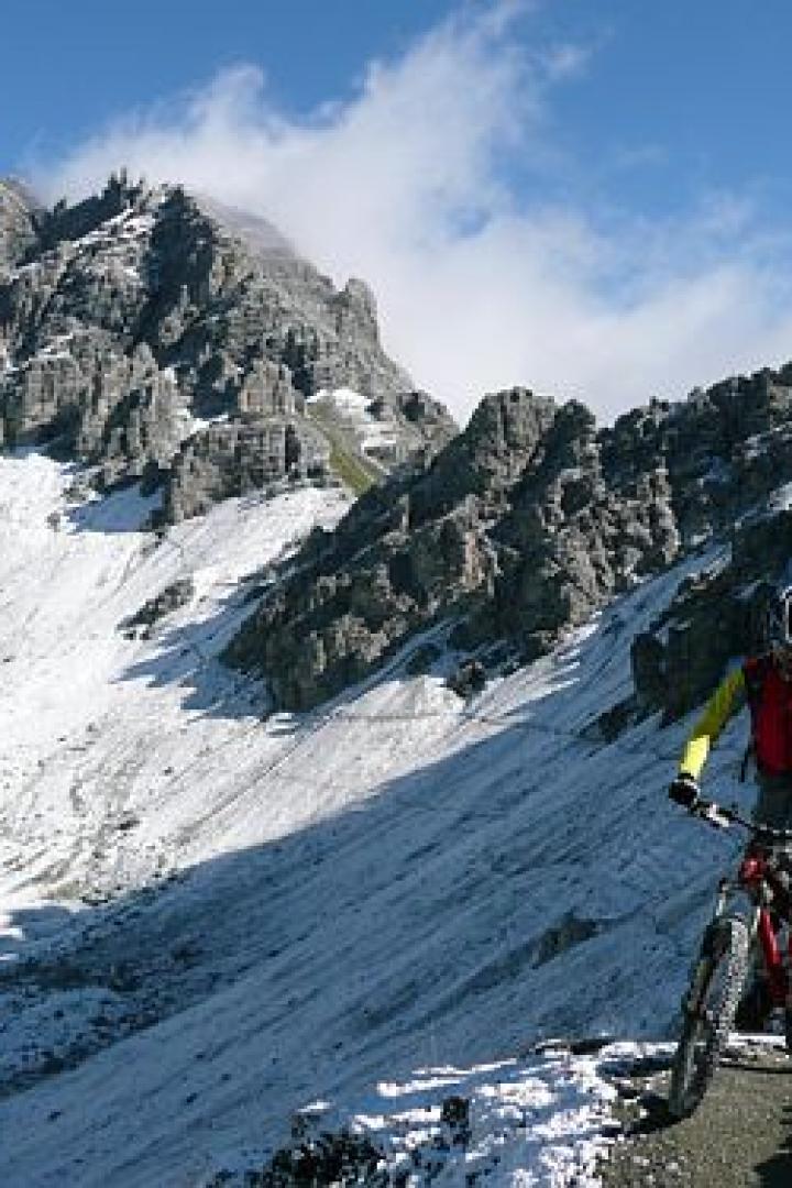 Ein Mountainbiker fährt auf einem Pfad in den verschneiten Bergen.