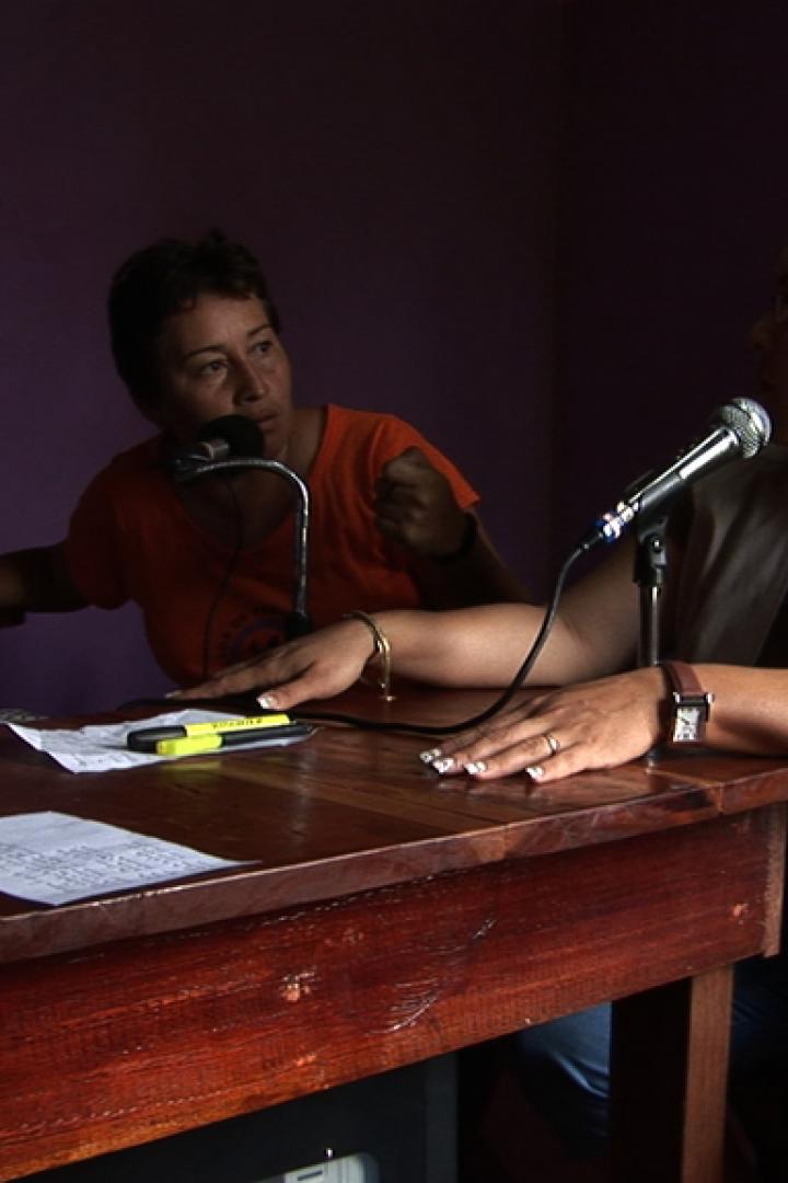 Zwei Frauen sitzen an einem Tisch mit Mikrofonen und sprechen.