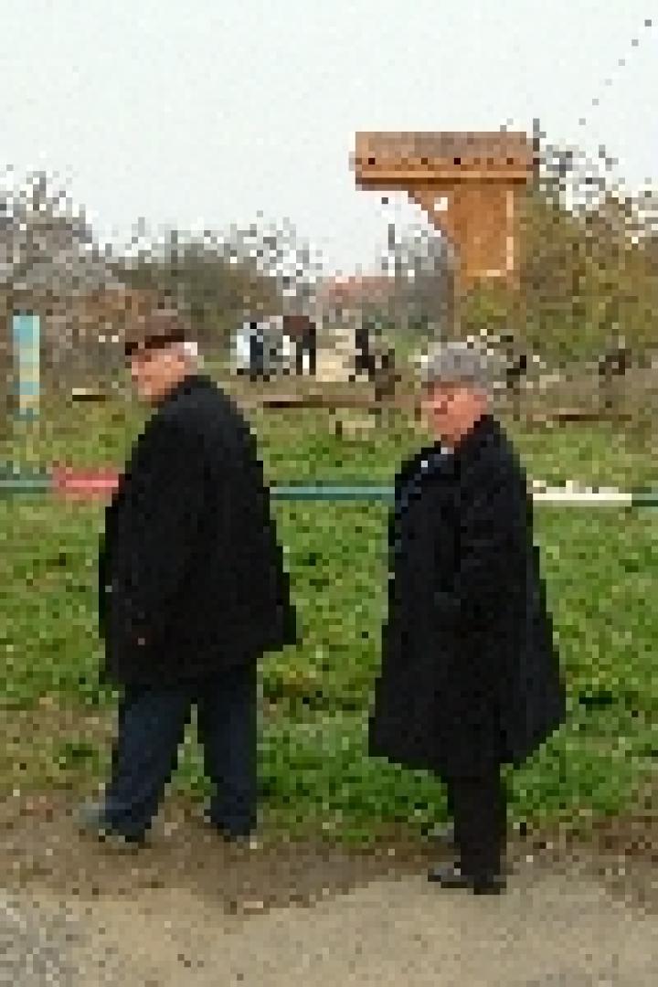 Zwei ältere Menschen stehen an einem Bahnübergang in einer ländlichen Gegend.