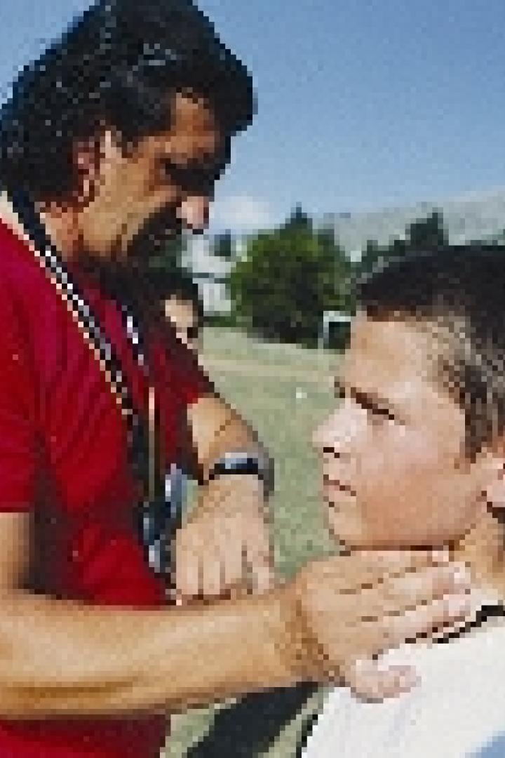 Ein Mann untersucht den Hals eines Jungen im Freien.