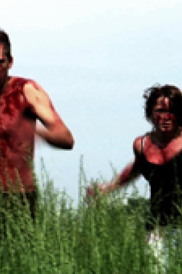 Mehrere blutverschmierte Menschen rennen durch hohes Gras.