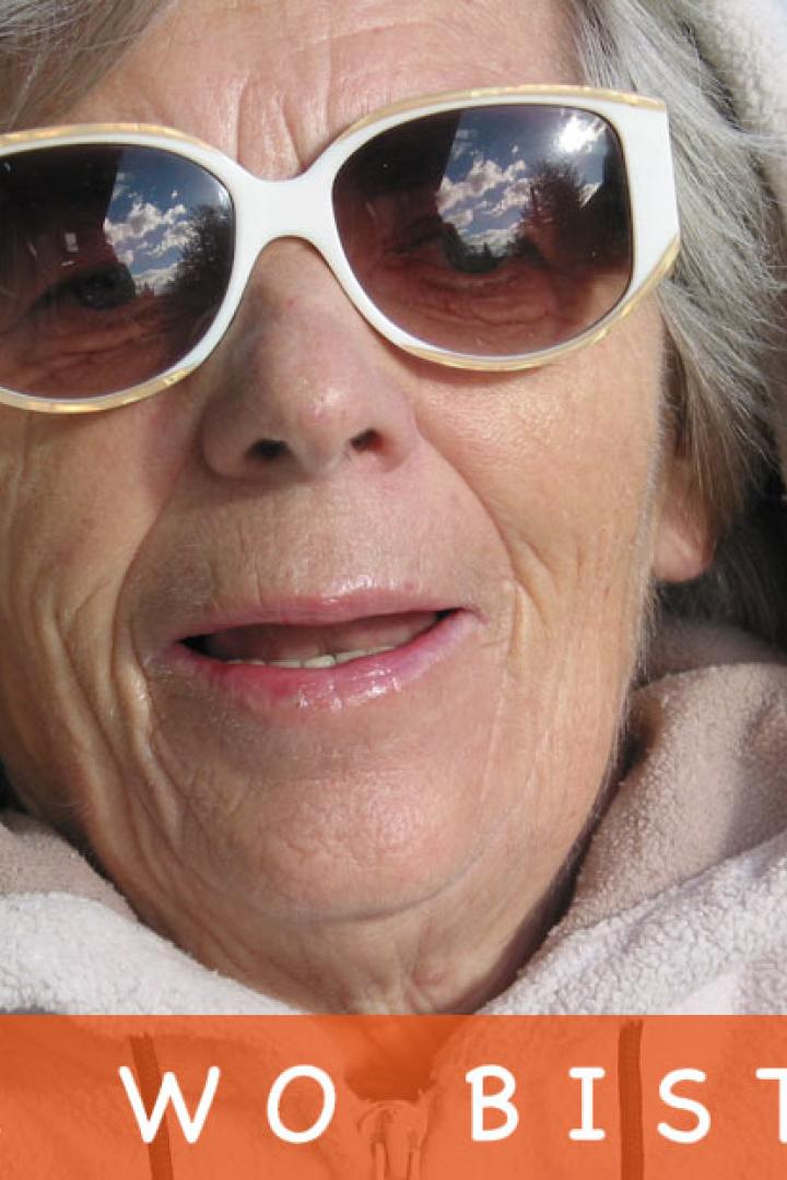 Eine ältere Frau mit Sonnenbrille und Kapuzenpullover liegt entspannt im Liegestuhl.