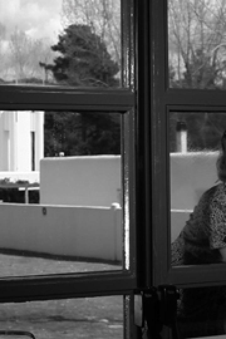 Eine Frau mit einem Tuch in der Hand schaut aus dem Fenster.