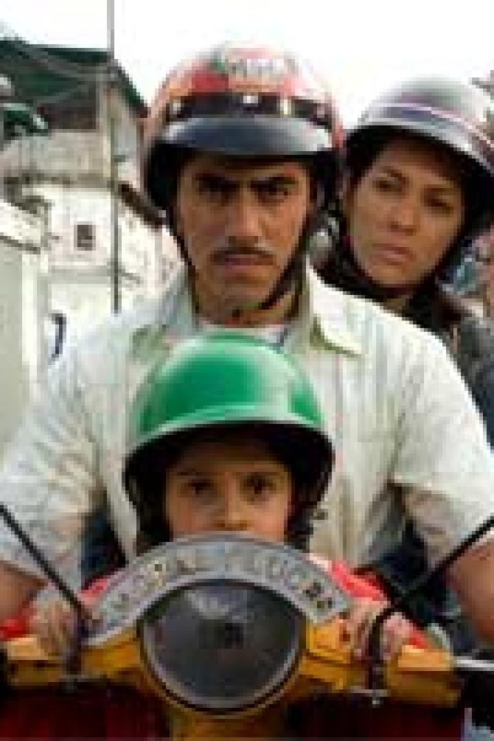 Ein Mann fährt mit einem Motorroller und transportiert ein Kind und eine Frau, alle mit Helmen.