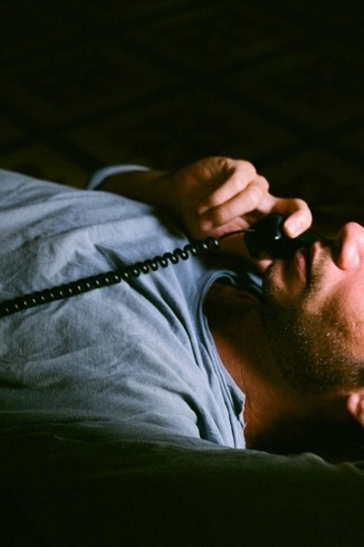 Ein Mann liegt auf dem Boden und telefoniert mit einem alten Telefon.