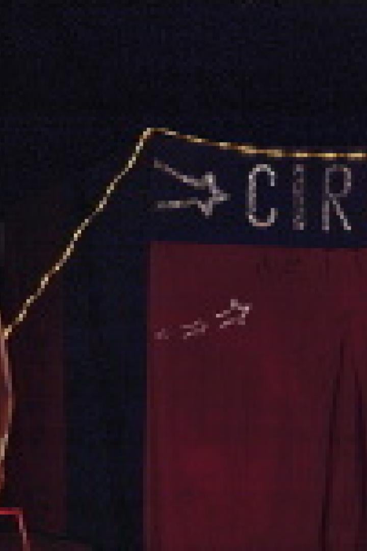 Eine Frau in einem weißen Badeanzug steht vor einem Zirkuszelt.