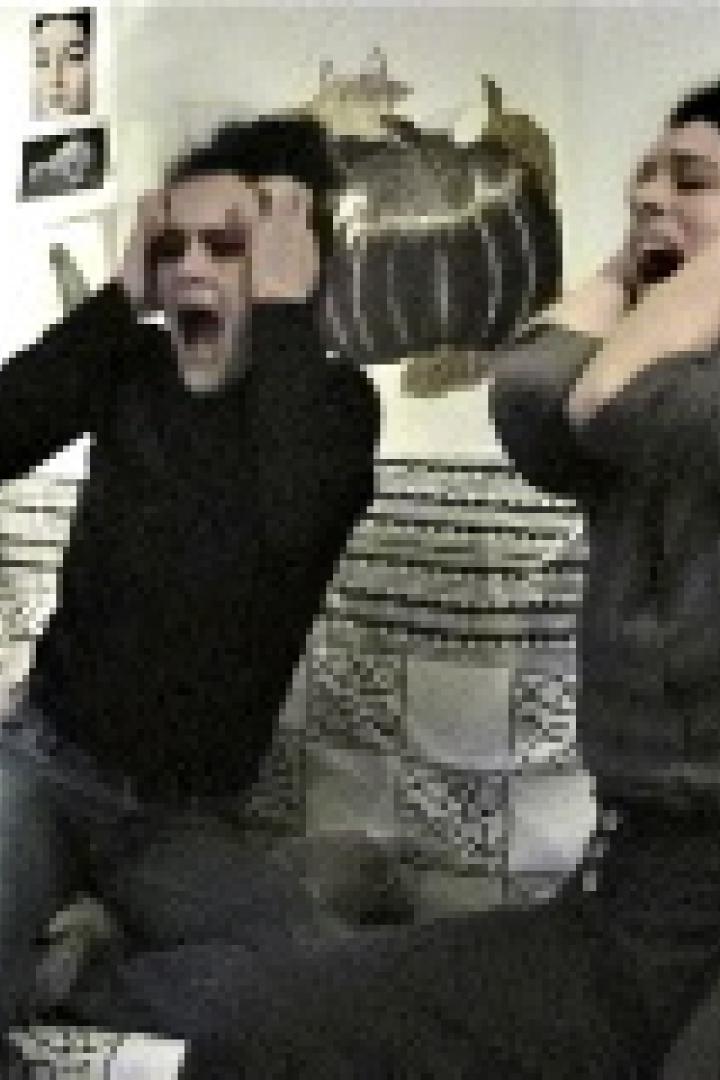 Zwei Personen sitzen auf einem Sofa und schreien mit den Händen an den Ohren.