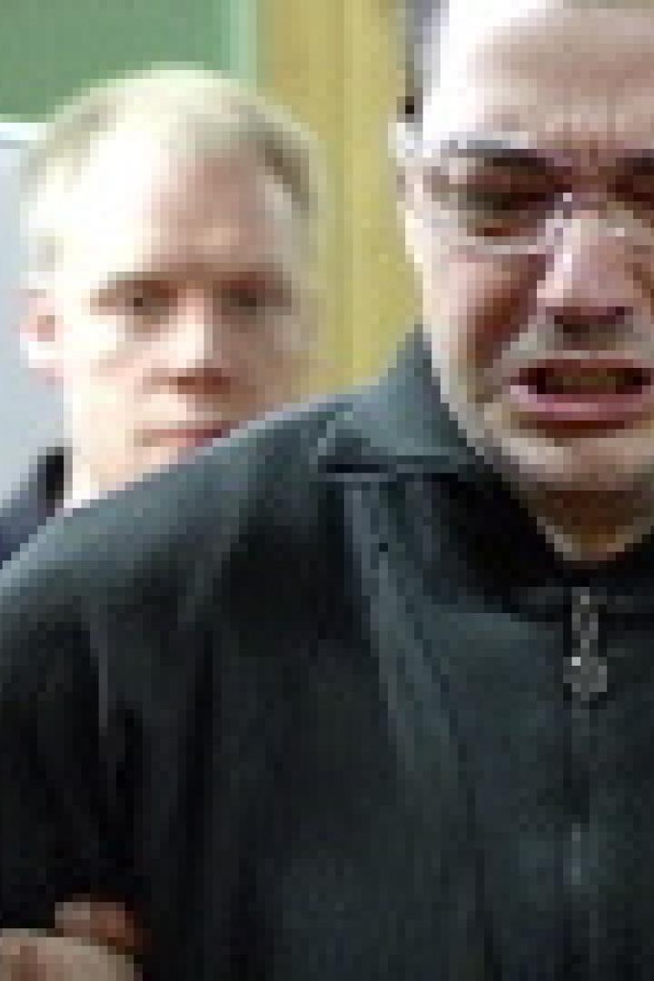 Ein Mann mit Schutzbrille verzieht schmerzhaft das Gesicht, umringt von anderen Männern.