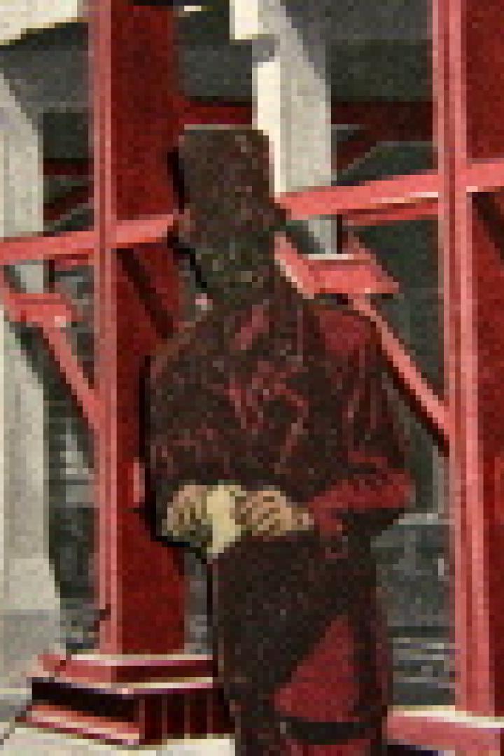 Eine stilisierte Figur mit Zylinder steht vor einem Gerüst aus roten Stahlträgern.