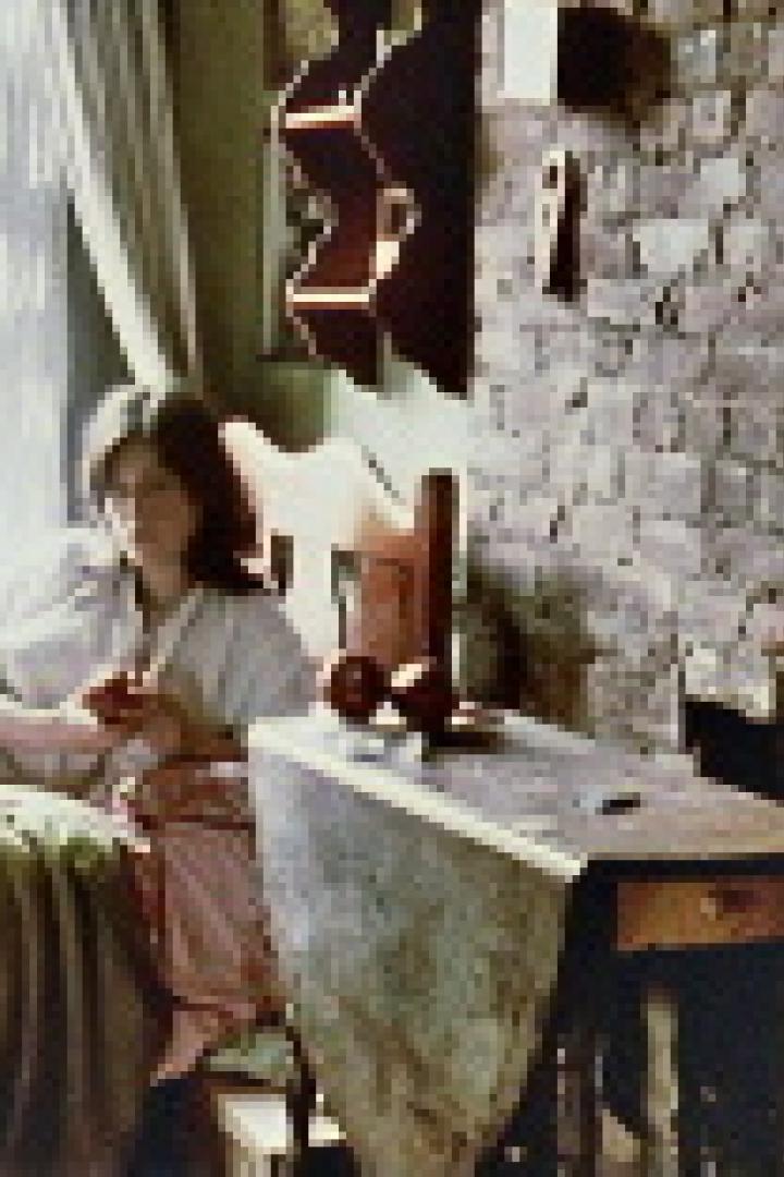 Eine junge Frau sitzt auf einem Bett und strickt in einem rustikalen Zimmer.