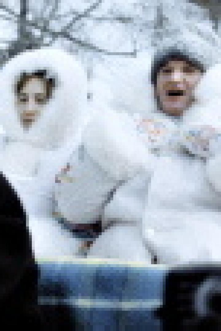 Ein Paar in dicken Winteranzügen sitzt in einem Schlitten im Schnee.