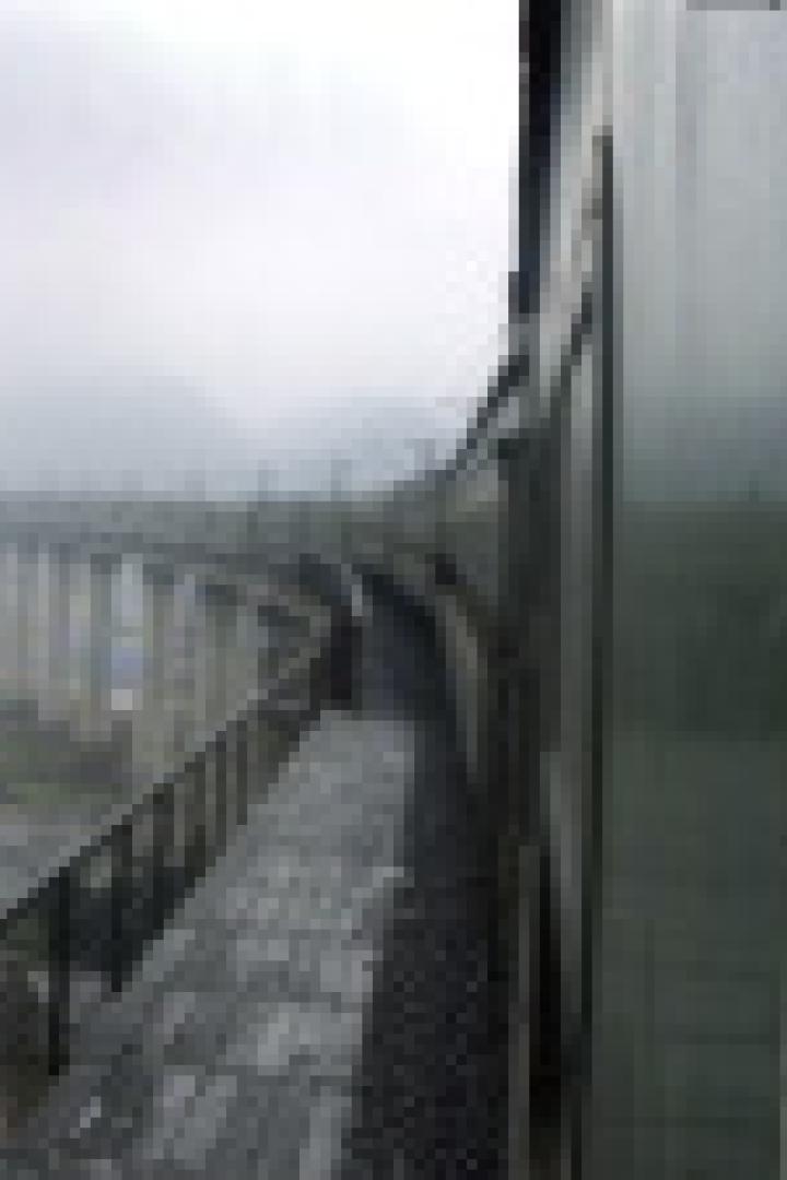 Ein Kind blickt aus dem Fenster eines Zuges auf eine Landschaft mit Bergen und einer Stadt.