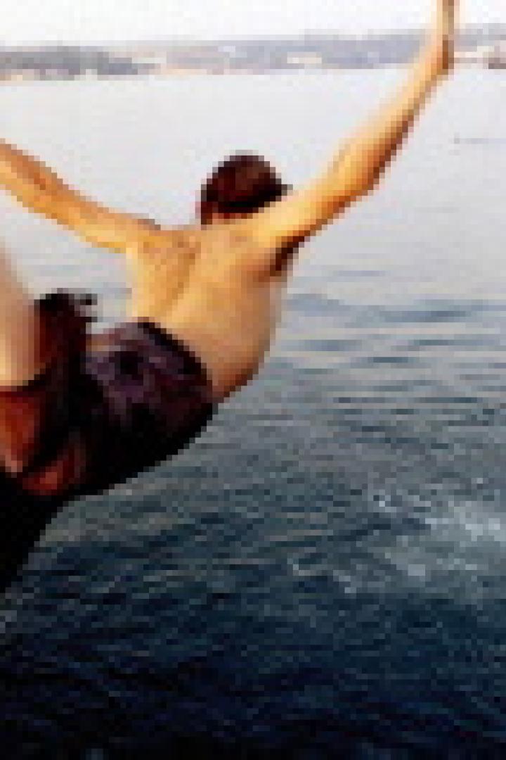 Ein Mann springt mit ausgestreckten Armen und Beinen ins Wasser.