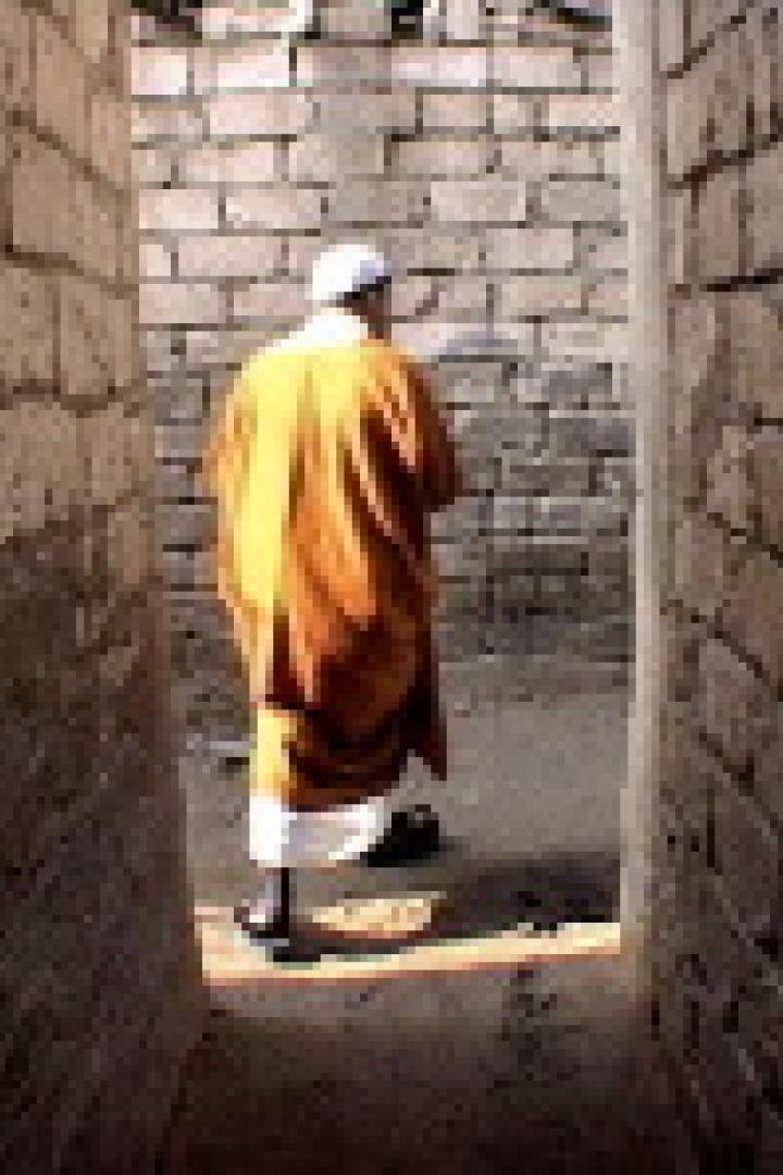 Ein Mann in orangefarbener Kleidung geht durch eine enge Gasse.