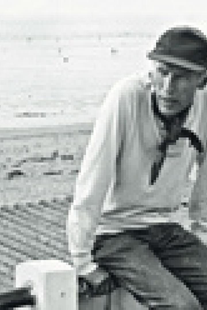 Ein Mann mit Mütze sitzt auf einer Mauer vor einer weiten Landschaft.