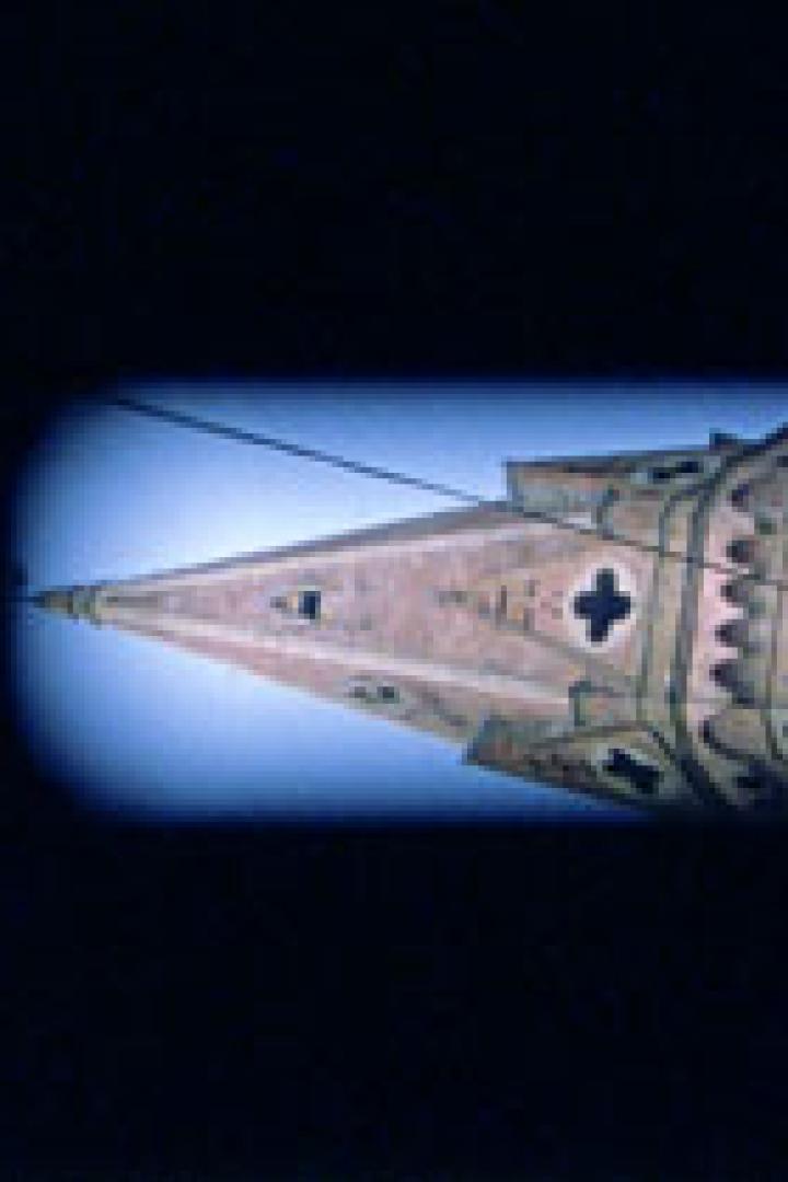 Detailaufnahme der Spitze eines Kirchturms vor blauem Himmel.