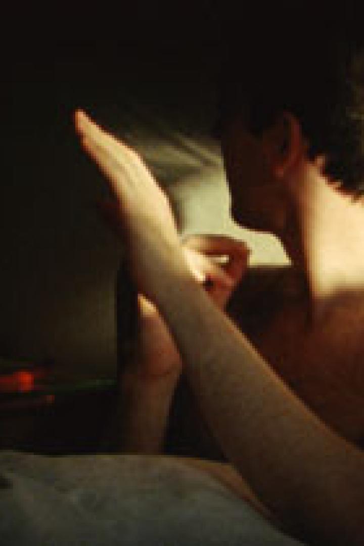 Ein Mann sitzt im Bett und hält eine Hand ins Licht.