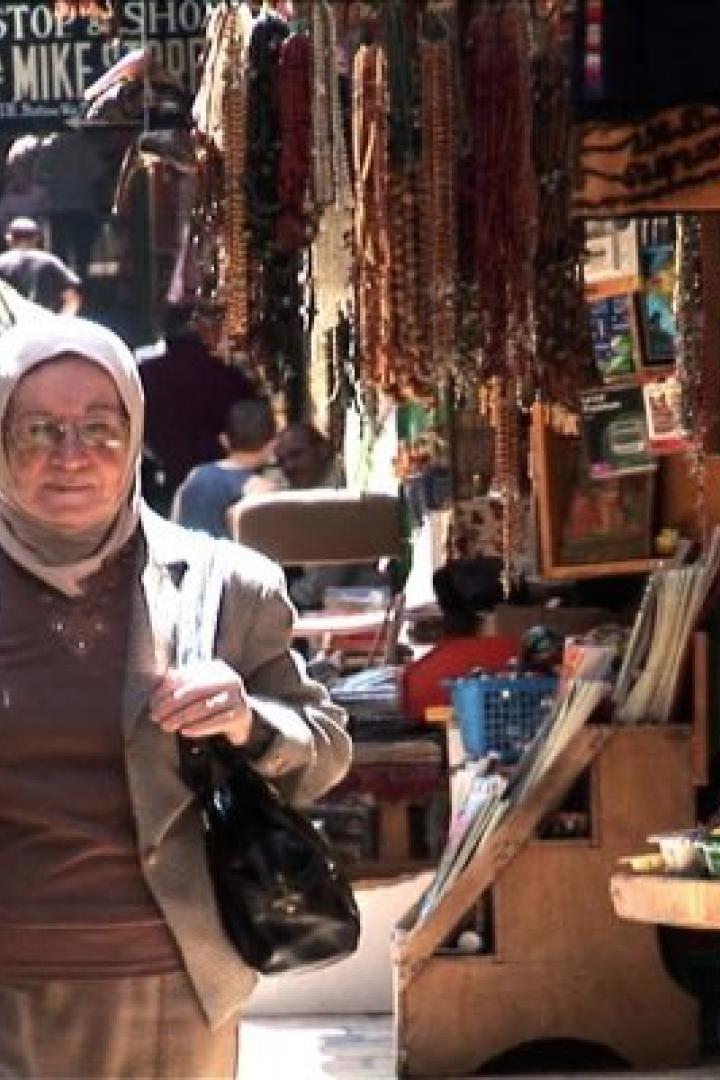 Eine Frau mit Kopftuch geht durch eine Gasse mit Verkaufsständen.