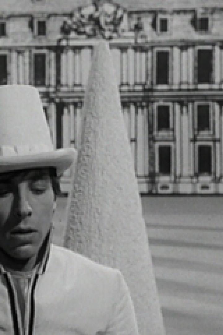 Ein Mann mit Zylinder und weißem Anzug vor einem gemalten Schloss.