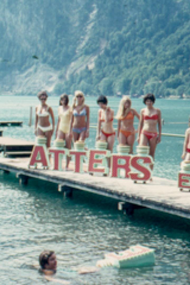 Eine Gruppe junger Frauen posiert mit dem Schriftzug „Attersee“ auf einem Steg im Wasser.