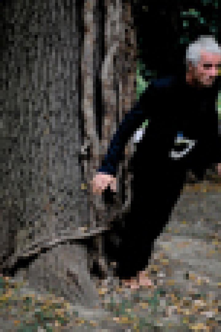 Ein Mann in schwarzer Kleidung lehnt an einem Baum in einem Park.