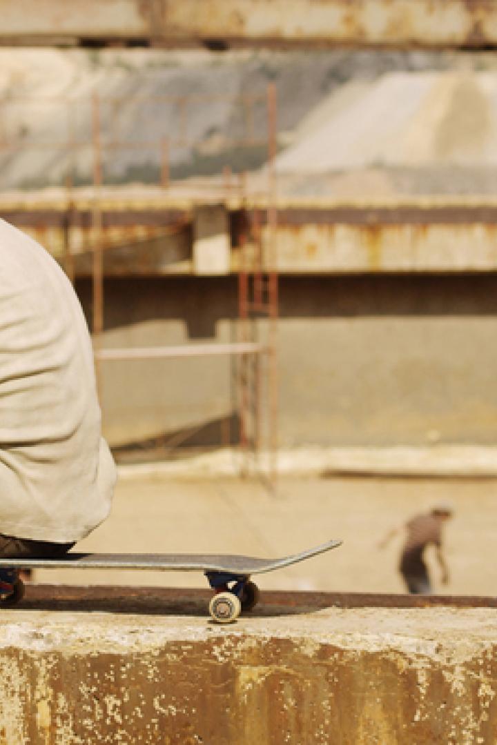 Ein junger Mann sitzt auf einem Skateboard und bindet seine Schuhe.