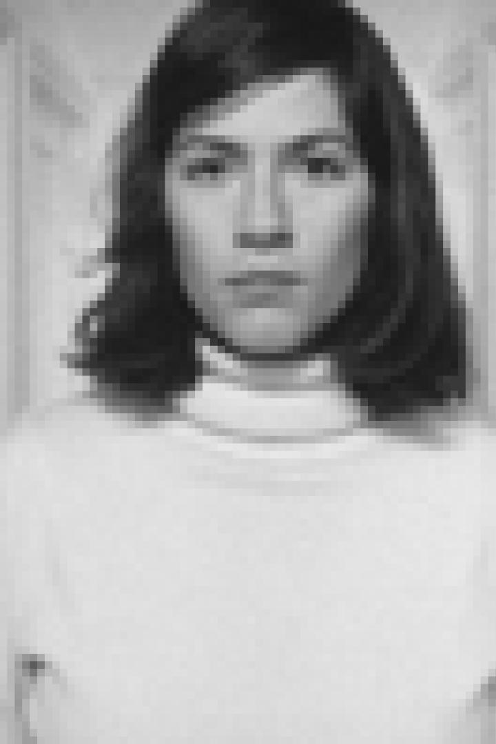 Eine Frau mit dunklen Haaren und einem weißen Rollkragenpullover steht in einem Flur.