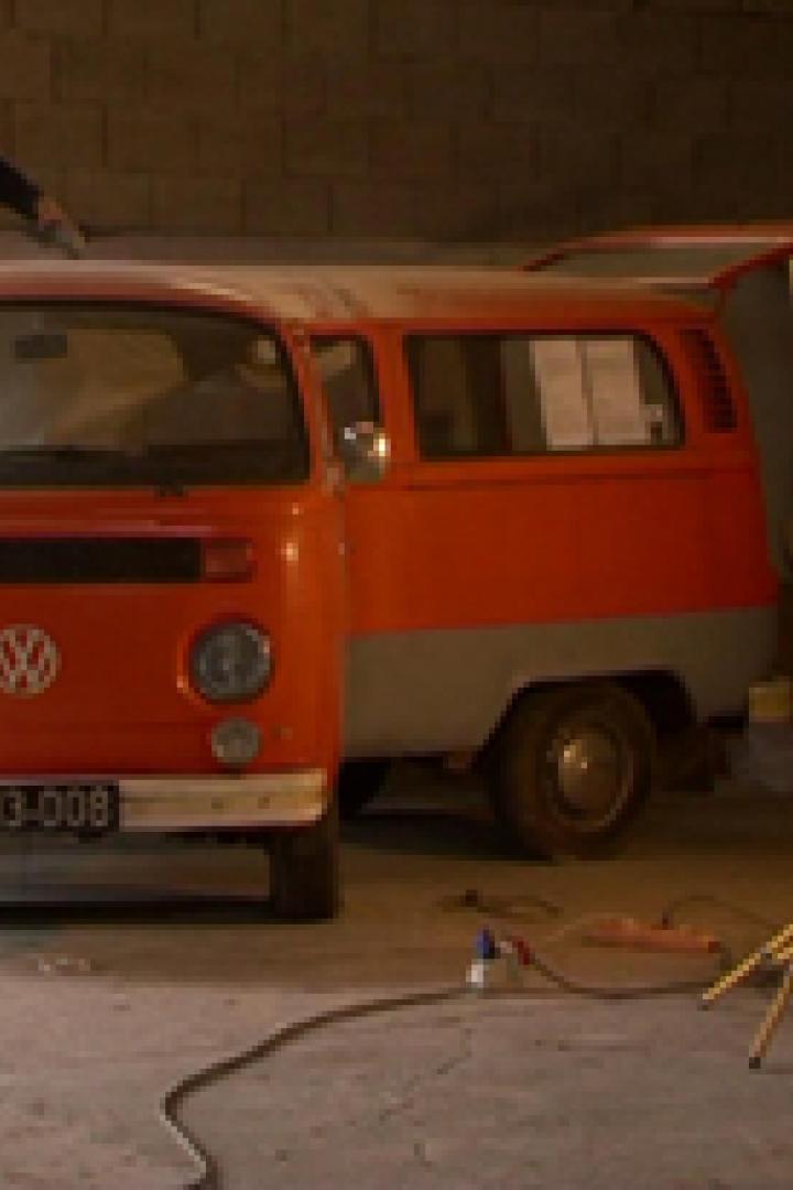 Eine orangefarbene VW-Kastenwagen wird in einer Werkstatt restauriert.
