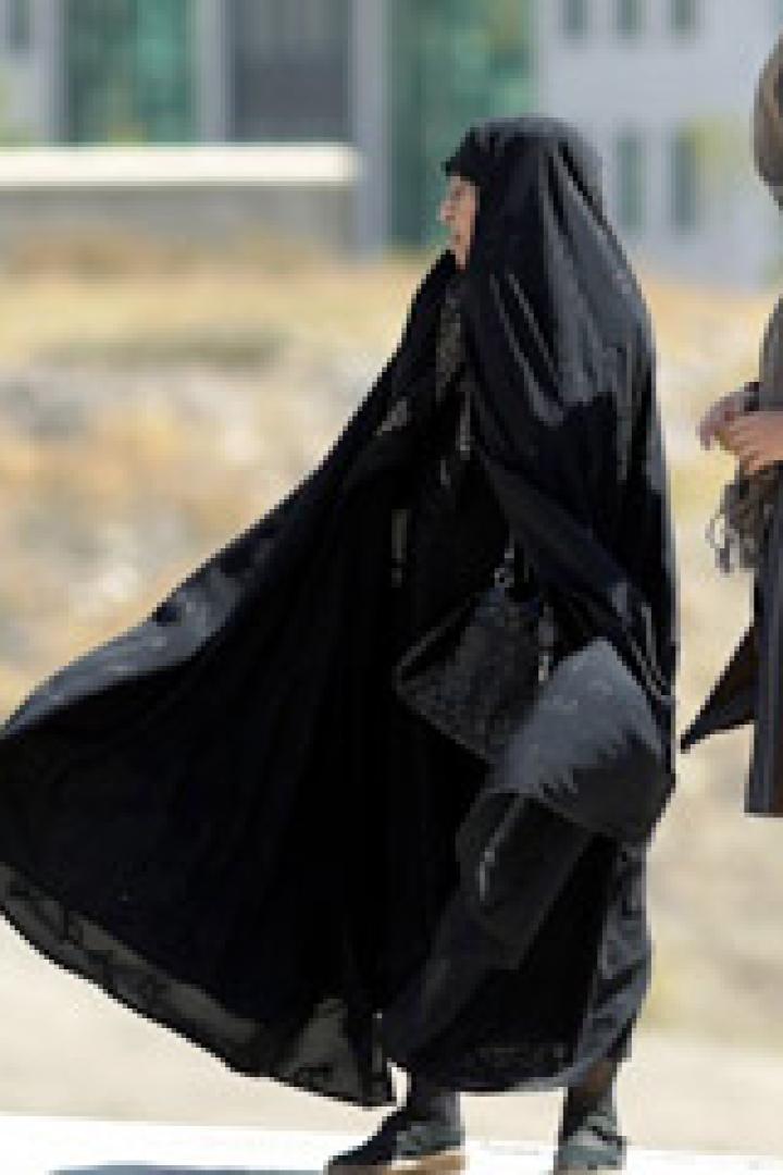 Zwei Frauen stehen im Freien, eine in traditioneller schwarzer Kleidung, die andere in moderner Kleidung.