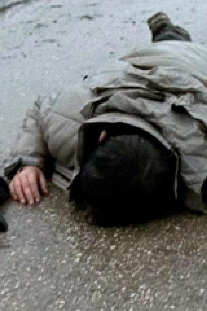 Eine Person liegt leblos auf einer nassen Straße.