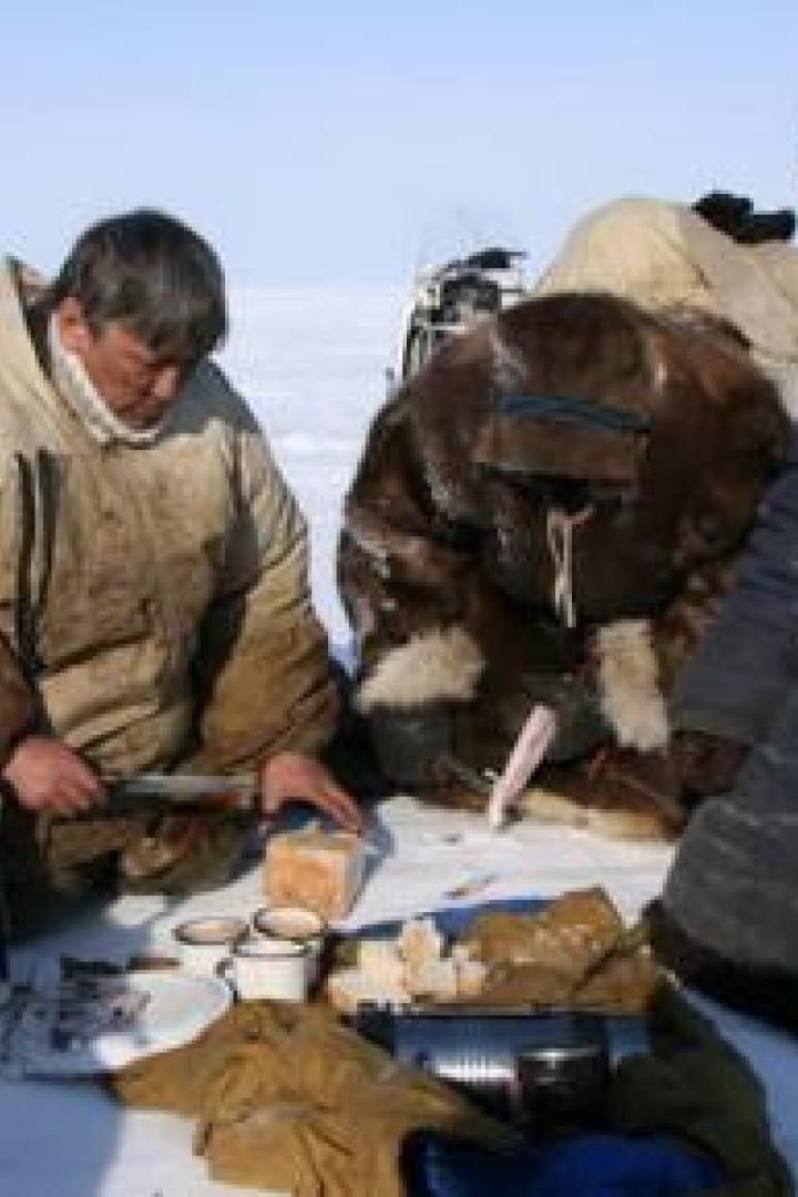 Eine Gruppe von Menschen macht im Schnee eine Pause und isst Brot.